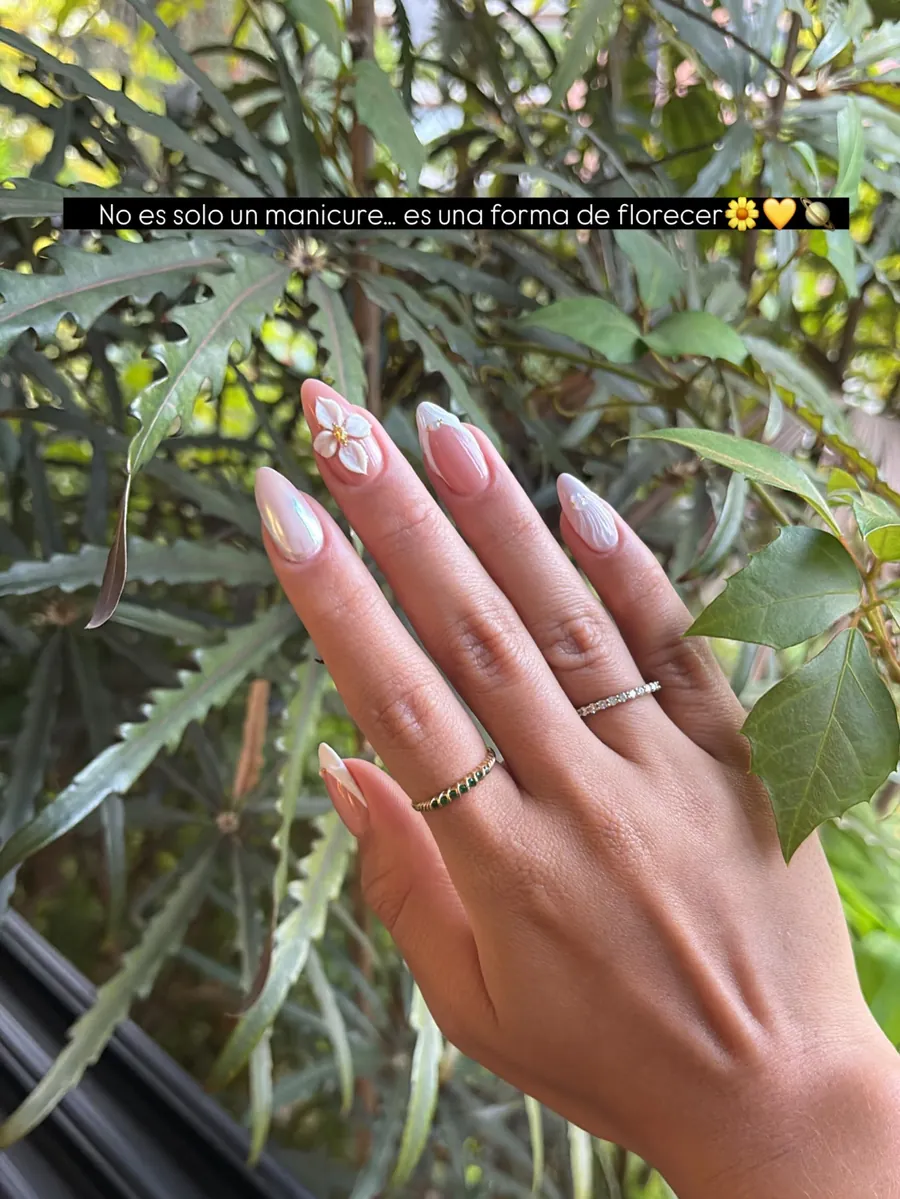 Uñas almendradas nude con detalle blanco, junto a una planta